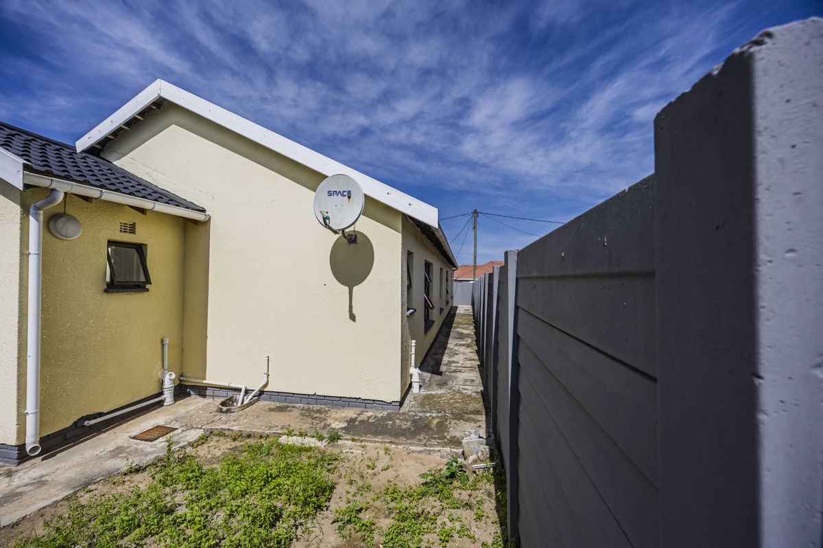 A side view of the property showing a concrete pathway, boundary wall, and exterior wall with a satellite dish installation.