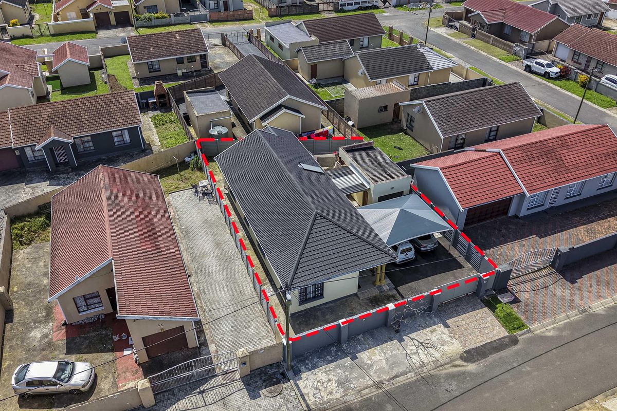Aerial view of a residential property featuring a tiled roof, paved driveway, carport, and secure boundary walling within a suburban neighborhood.