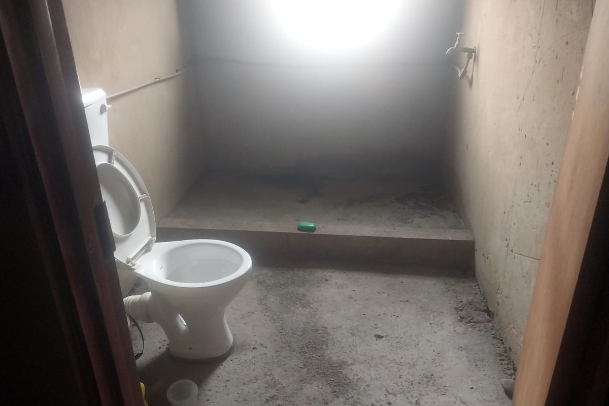 A basic, unfinished bathroom space featuring a toilet and wall-mounted faucet, requiring significant renovation and finishing of walls and flooring.