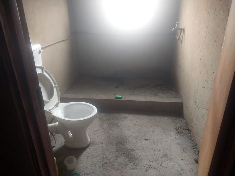 A basic, unfinished bathroom space featuring a toilet and wall-mounted faucet, requiring significant renovation and finishing of walls and flooring.