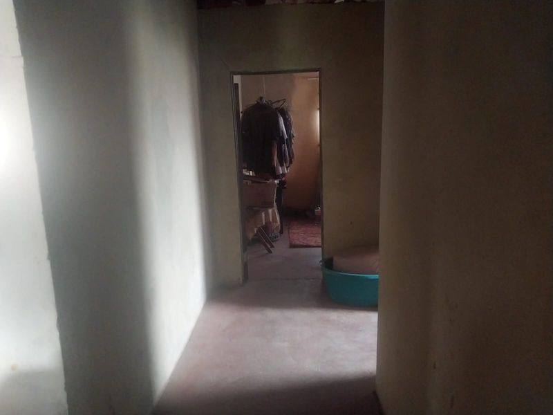 A dimly lit, narrow hallway with basic wall finishes and concrete flooring, leading into an adjacent room.