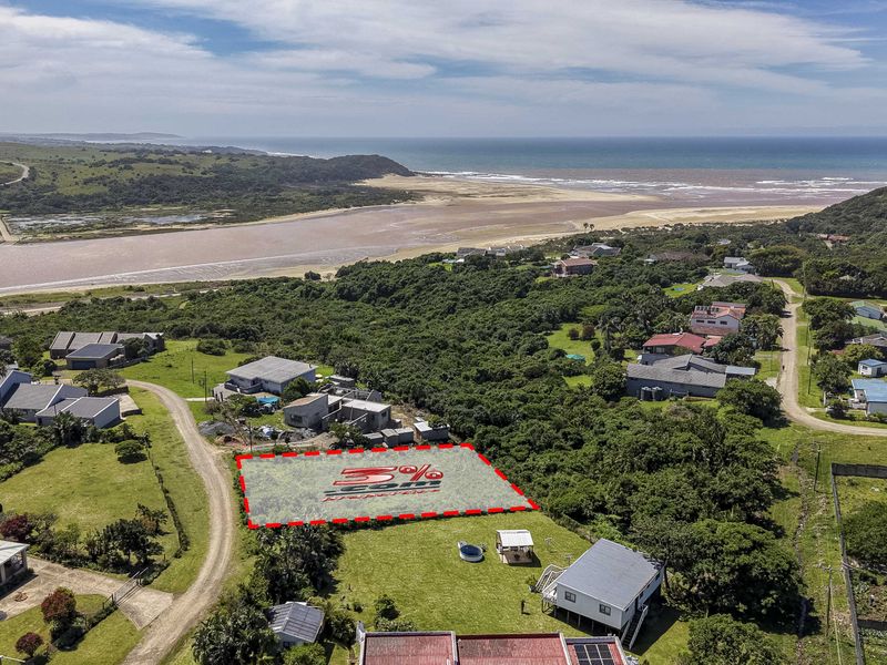 Aerial view of a vacant residential plot situated in a coastal area with surrounding natural vegetation and nearby residential properties.