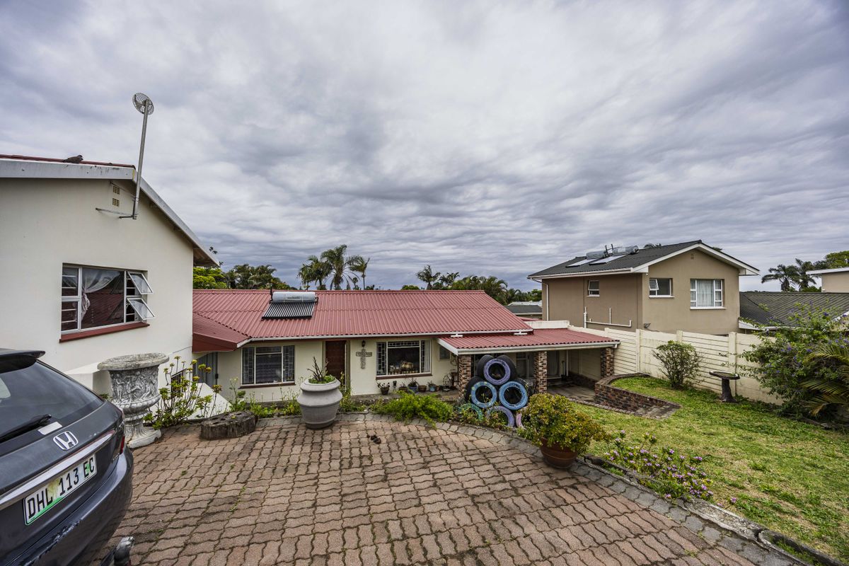 Rear view of the property featuring a corrugated metal roof with solar water heating, a brick-paved driveway, and a landscaped garden area.