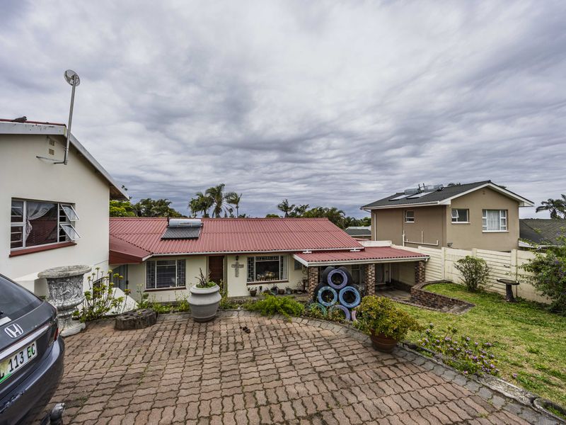 Rear view of the property featuring a corrugated metal roof with solar water heating, a brick-paved driveway, and a landscaped garden area.