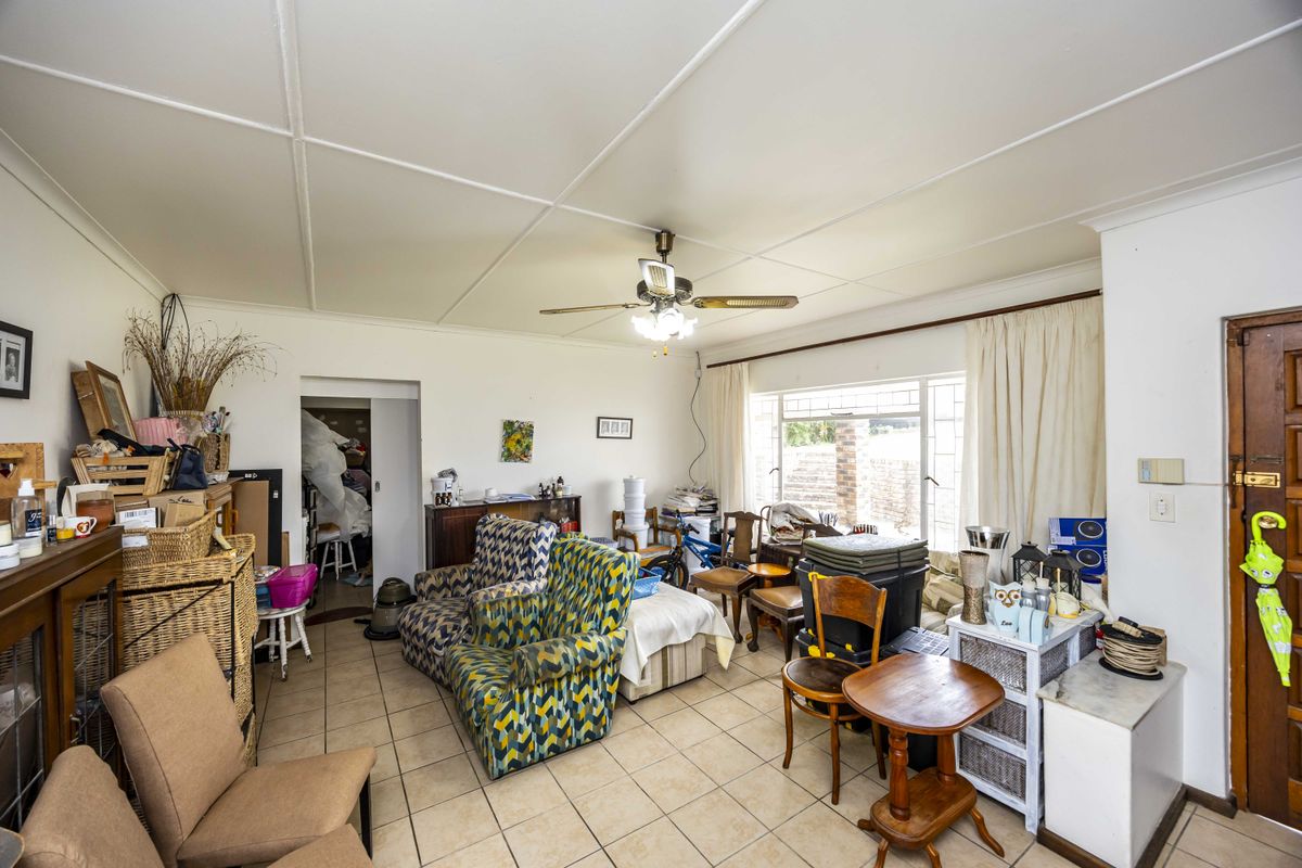A living room featuring tiled flooring, a ceiling fan, and large windows, currently requiring cosmetic updates and decluttering to improve the space.