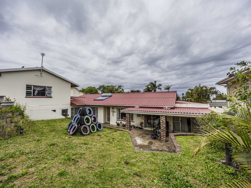 Rear view of the house featuring a corrugated metal roof, solar water heater, and a paved patio area with brick pillars.