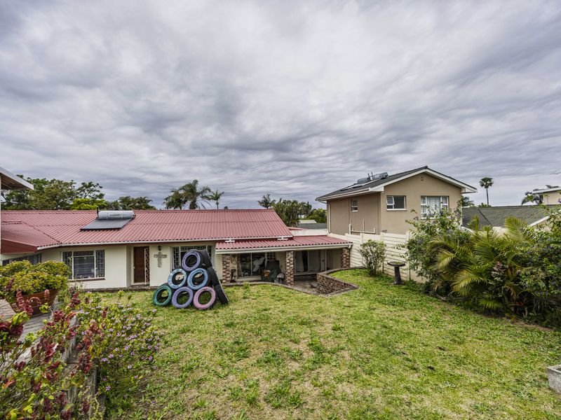 Rear view of the property featuring a lawn, paved patio area, and a corrugated metal roof with an integrated solar water heating system.