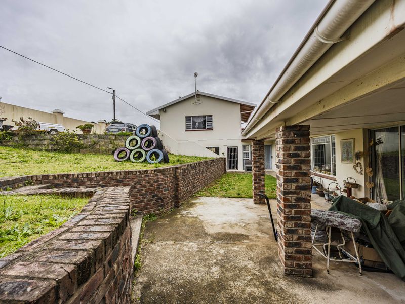 Rear exterior view featuring a covered patio with brick columns, concrete flooring, and a tiered garden with brick retaining walls.