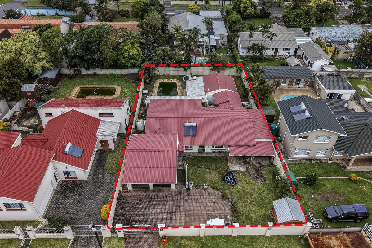 Aerial view of a residential property featuring a metal roof, paved driveway, swimming pool, and a fenced garden area.