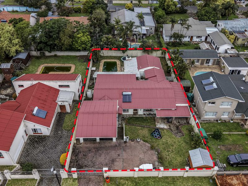 Aerial view of a residential property featuring a metal roof, paved driveway, swimming pool, and a fenced garden area.