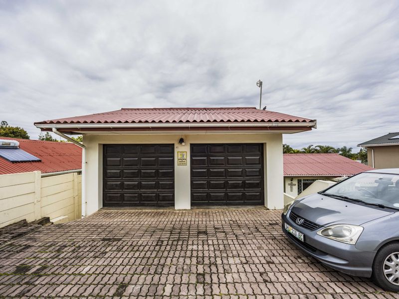 A detached double garage featuring dark panelled doors, a red corrugated roof, and a paved driveway area.