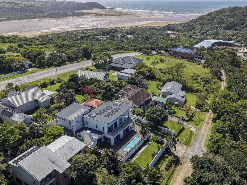 Aerial view of a coastal property featuring a swimming pool, solar panels, and landscaped grounds, situated in a scenic seaside location.