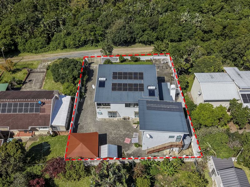 Aerial view of the property showing the main dwelling with solar panels, paved driveway, and surrounding garden area within the boundary.