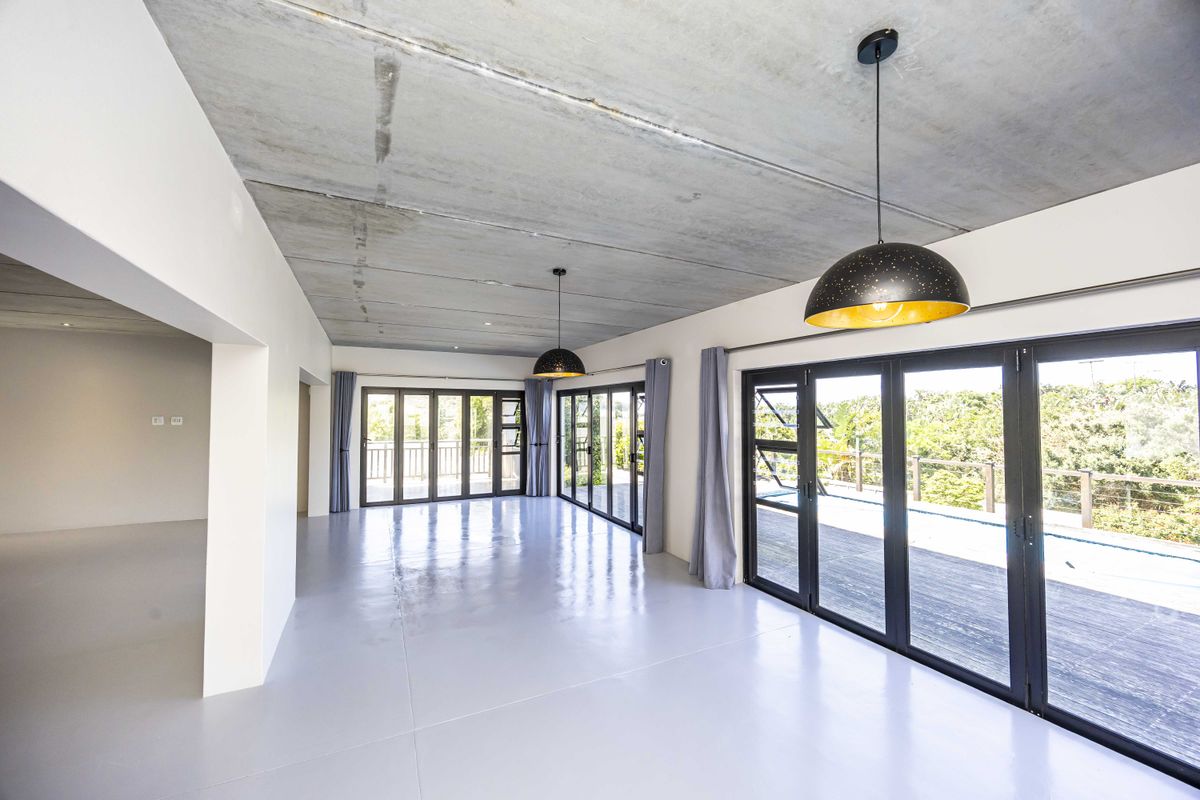 Spacious open-plan living area featuring an exposed concrete ceiling, polished epoxy flooring, and large aluminium stacker doors opening onto an outdoor deck.