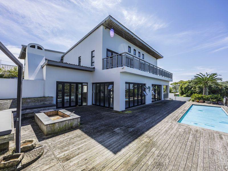 Rear exterior view featuring a swimming pool, expansive timber decking, a built-in fire pit, and a balcony overlooking the outdoor entertainment area.