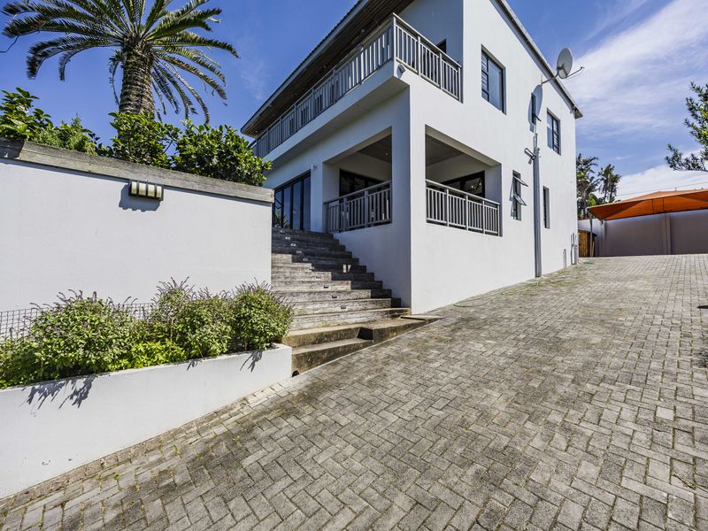 A multi-level residential exterior featuring a paved driveway, concrete staircase leading to the entrance, and balcony railings on the upper level.