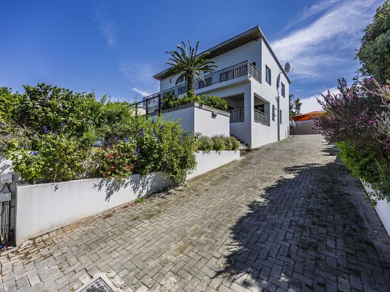 A well-maintained multi-story house featuring a paved driveway, landscaped garden beds, and a balcony with metal railings.