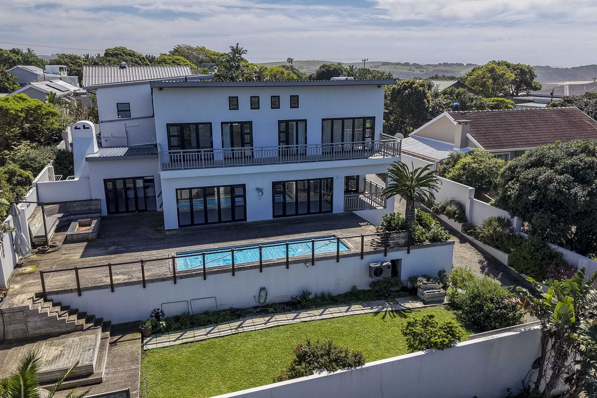 Aerial view of the rear property elevation featuring a swimming pool, timber deck, outdoor fireplace, and a spacious balcony overlooking the garden.