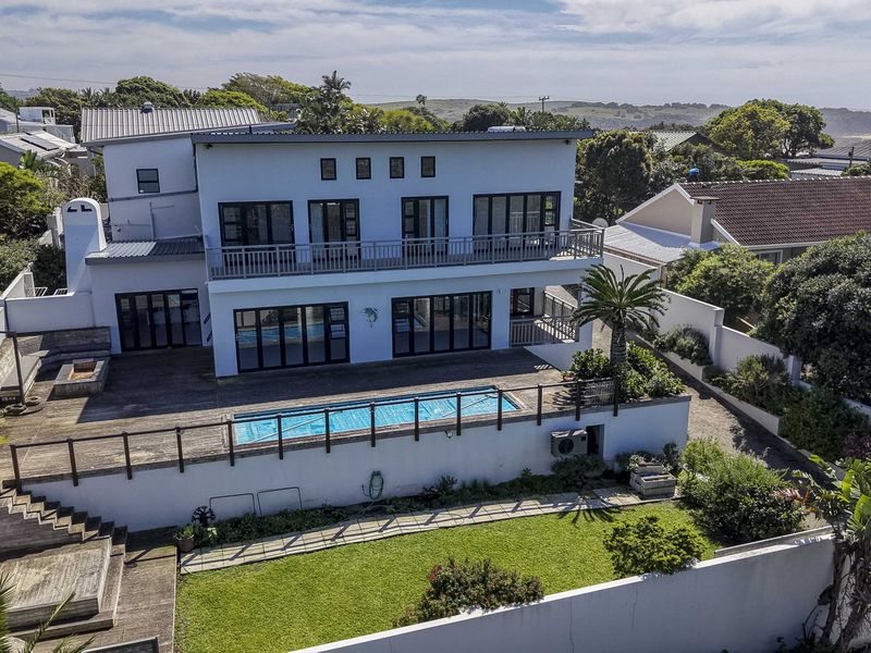 Aerial view of the rear property elevation featuring a swimming pool, timber deck, outdoor fireplace, and a spacious balcony overlooking the garden.