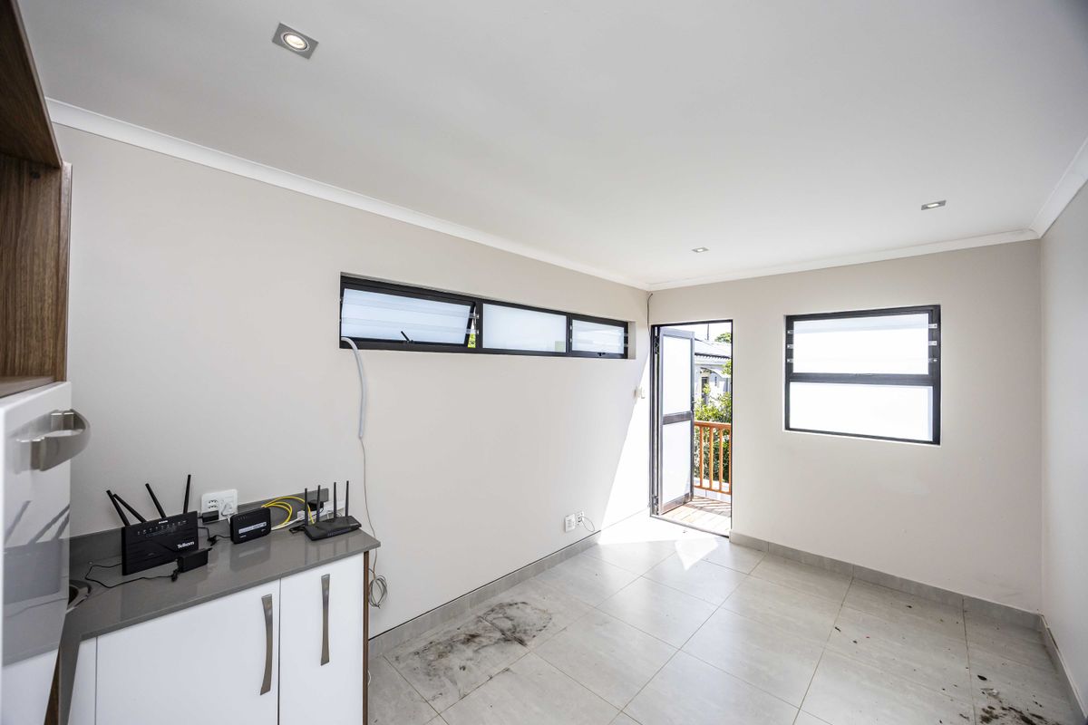 A bright, empty kitchen area featuring tiled flooring, built-in cabinetry with stone countertops, and direct access to an outdoor balcony.