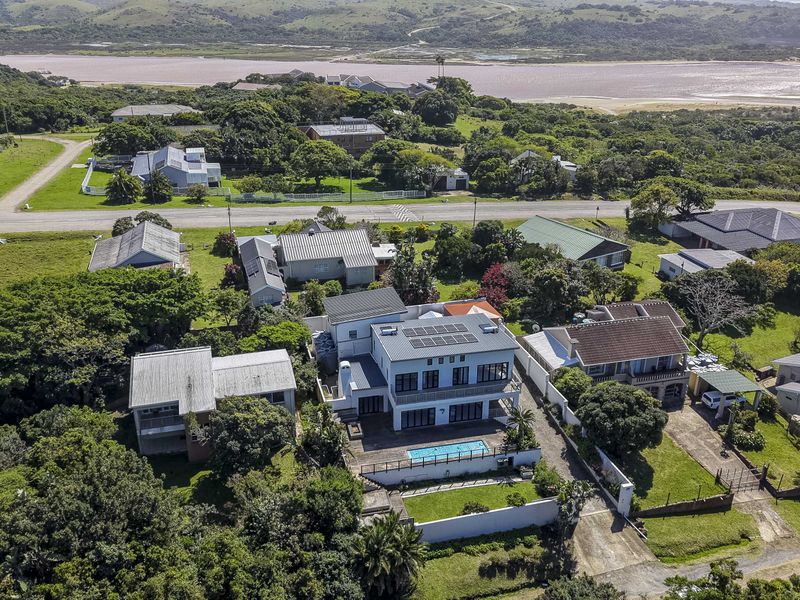 Aerial view of a coastal residential property featuring a swimming pool, solar panels, and landscaped grounds in a scenic neighborhood setting.