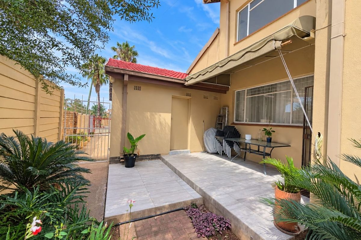 A well-maintained rear patio area featuring tiled flooring, a retractable awning, and direct access to the garden and side gate.