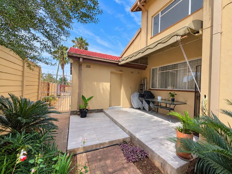 A well-maintained rear patio area featuring tiled flooring, a retractable awning, and direct access to the garden and side gate.