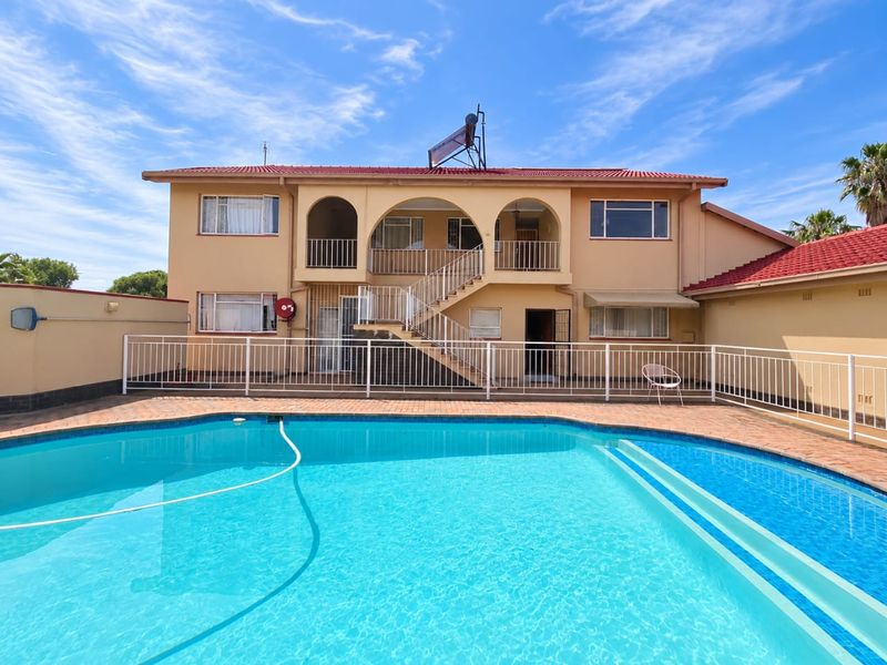 A well-maintained apartment complex exterior featuring a swimming pool, paved deck, and an external staircase leading to upper-level units.