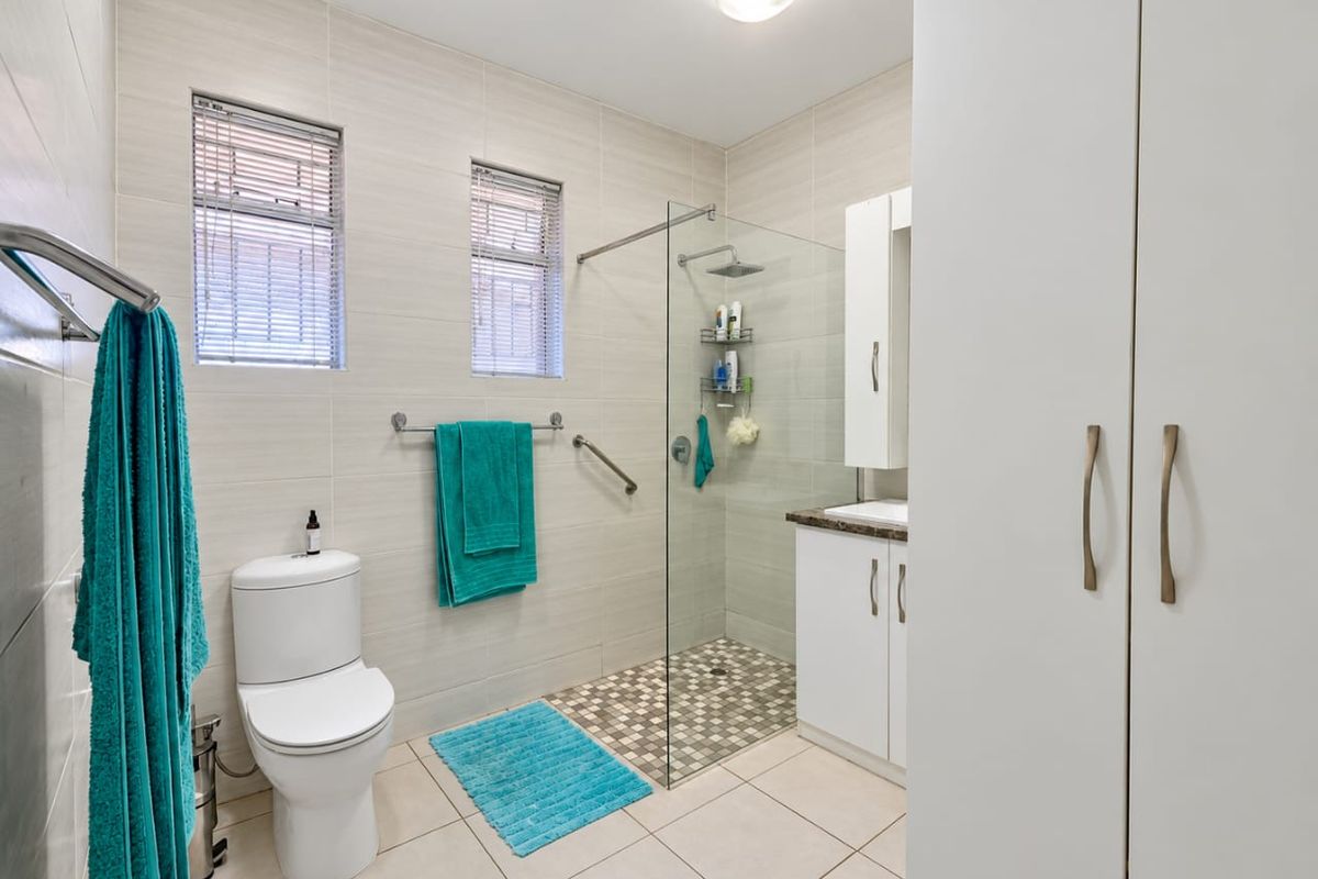 Modern bathroom featuring a walk-in shower with glass screen, vanity cabinet, built-in storage cupboards, and neutral wall and floor tiling.