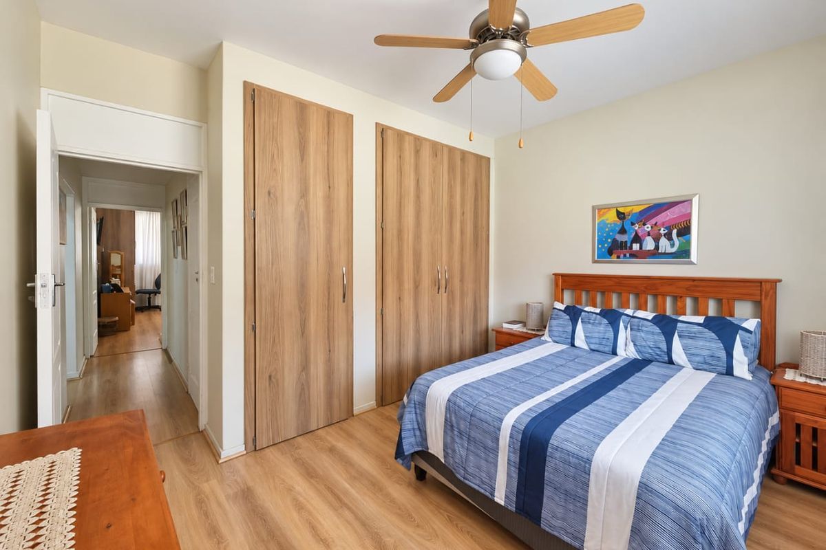 A well-maintained bedroom featuring laminate flooring, built-in wooden cupboards, and a ceiling fan, offering a clean and functional living space.