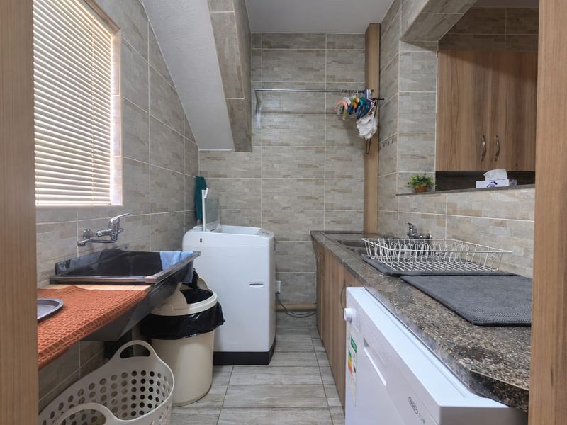 A functional laundry room featuring tiled walls and flooring, built-in cabinetry with stone countertops, and a stainless steel sink.