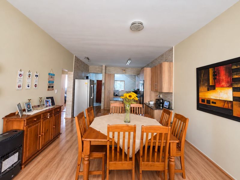 Open plan dining area flowing into a functional kitchen with wood-look cabinetry, stone countertops, and laminate flooring throughout.
