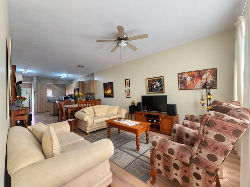 Spacious open-plan living and dining area featuring laminate flooring, a ceiling fan, and a functional kitchen with built-in cabinetry.