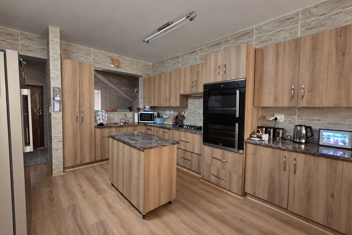 Modern kitchen featuring wood-grain cabinetry, stone-look countertops, a central island, and integrated double oven, complemented by stylish wall tiling and laminate flooring.