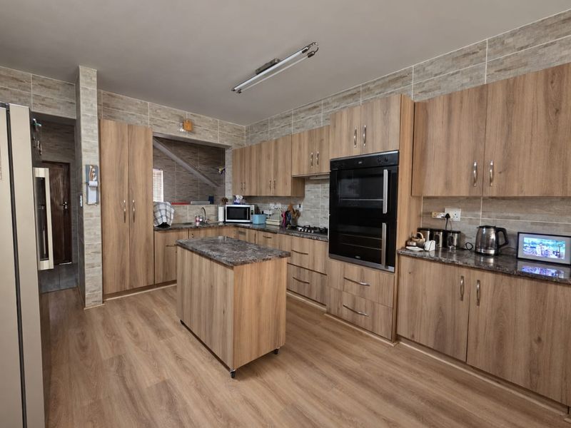 Modern kitchen featuring wood-grain cabinetry, stone-look countertops, a central island, and integrated double oven, complemented by stylish wall tiling and laminate flooring.