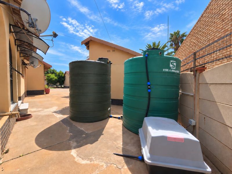 Rear exterior area featuring two large water storage tanks, concrete paving, and perimeter walling.