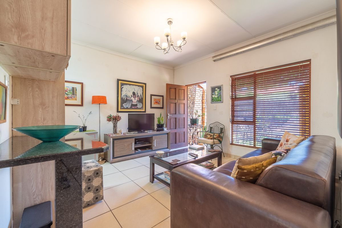 A cozy living room featuring tiled flooring, a wooden entrance door, and venetian blinds, offering a functional space with direct access to the exterior.