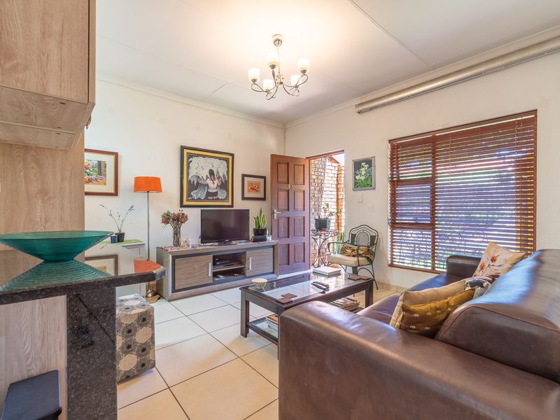A cozy living room featuring tiled flooring, a wooden entrance door, and venetian blinds, offering a functional space with direct access to the exterior.