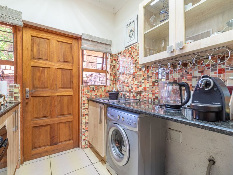 Compact scullery featuring granite countertops, vibrant mosaic tile backsplash, built-in cabinetry, and dedicated plumbing for laundry appliances.