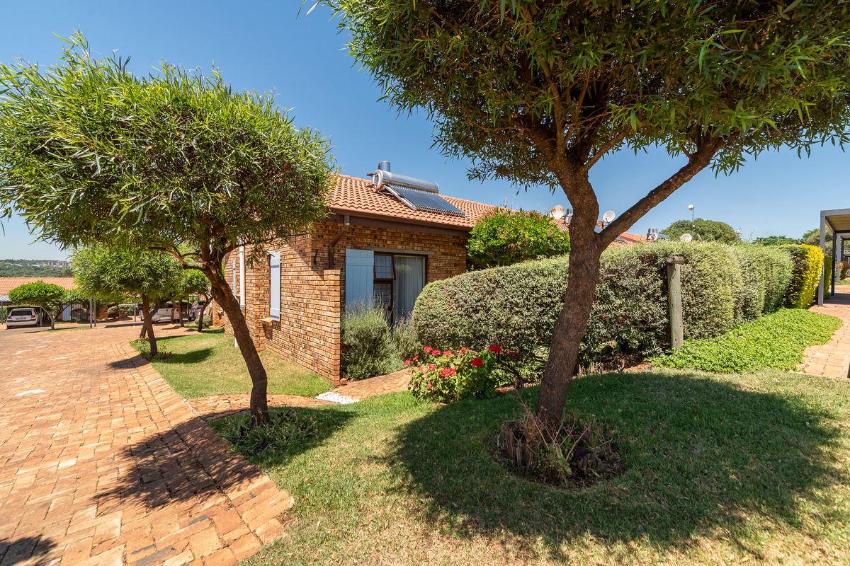 A well-maintained townhouse exterior featuring face brick construction, a tiled roof with a solar water heater, and a landscaped garden with paved pathways.