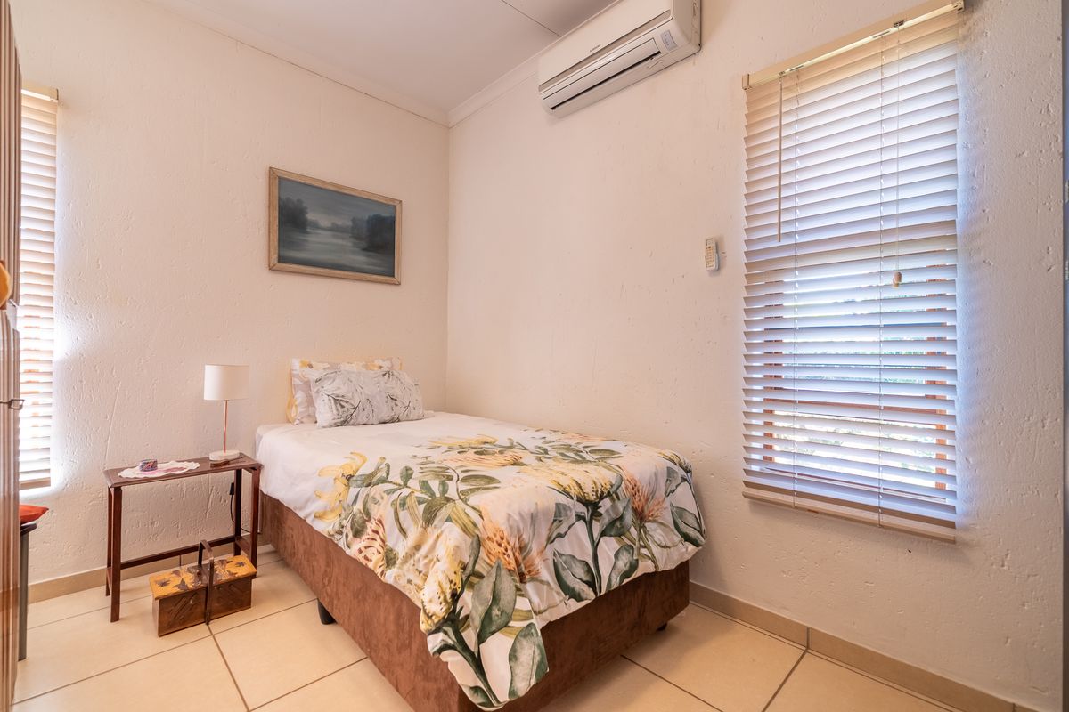 A functional bedroom featuring tiled flooring, dual windows with venetian blinds, and a wall-mounted split-system air conditioning unit.