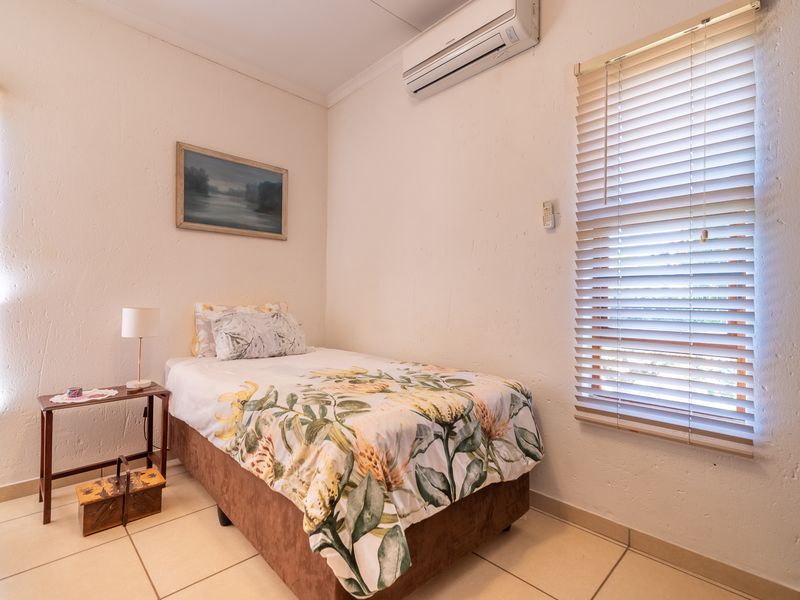 A functional bedroom featuring tiled flooring, dual windows with venetian blinds, and a wall-mounted split-system air conditioning unit.