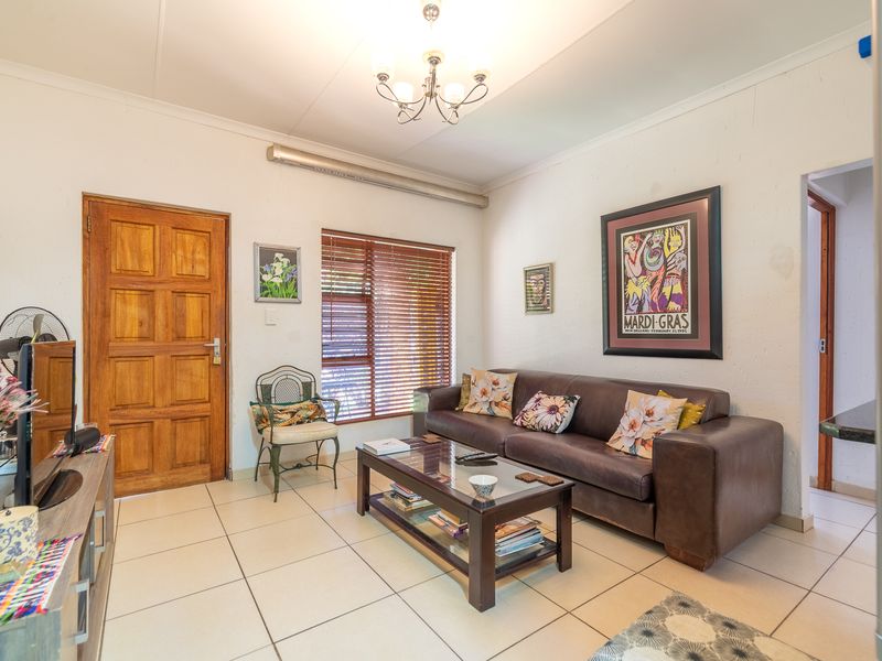 A living room featuring tiled flooring, a solid wooden door, and venetian blinds, providing a functional and well-lit space.