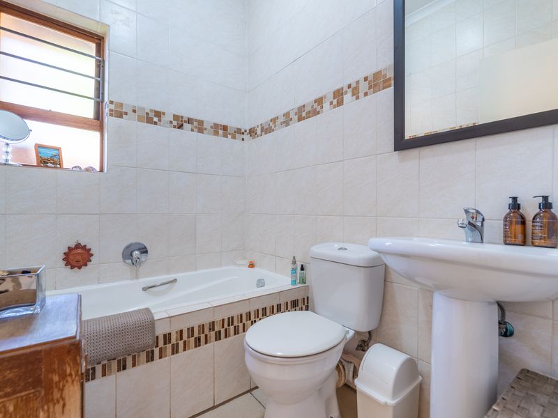 A functional bathroom featuring a bathtub, pedestal basin, and toilet, finished with neutral wall tiles and decorative mosaic accents.