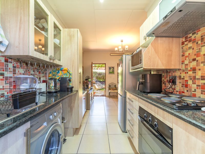 Galley-style kitchen featuring light wood cabinetry, granite countertops, mosaic tile backsplash, and integrated appliances, leading directly to an outdoor area.