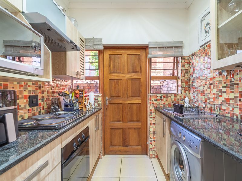 Compact galley-style kitchen featuring granite countertops, mosaic tile backsplash, built-in oven, electric hob, and integrated cabinetry with direct access to the exterior.
