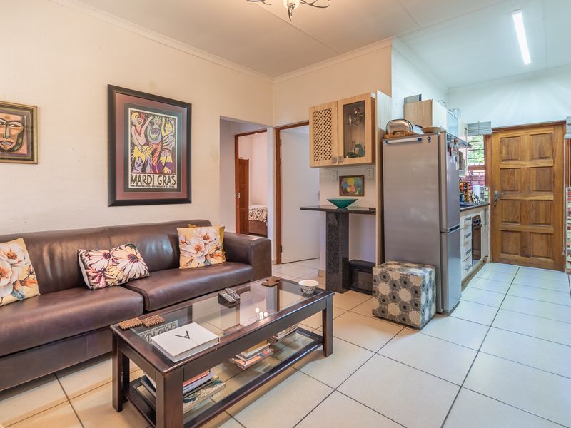 Open-plan living area featuring tiled flooring and a compact kitchen with built-in cabinetry, oven, and hob, leading to a timber entrance door.