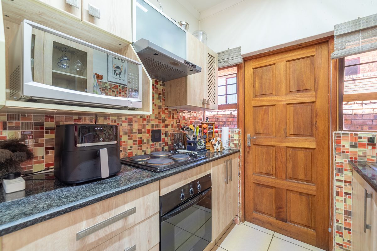 A compact kitchen featuring light wood cabinetry, granite countertops, a built-in oven with hob, and a vibrant mosaic tiled backsplash.