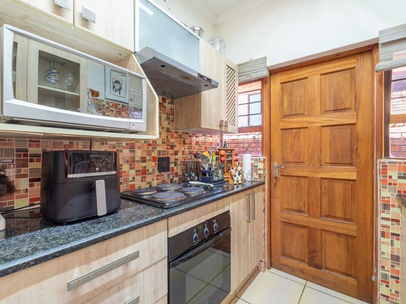 A compact kitchen featuring light wood cabinetry, granite countertops, a built-in oven with hob, and a vibrant mosaic tiled backsplash.