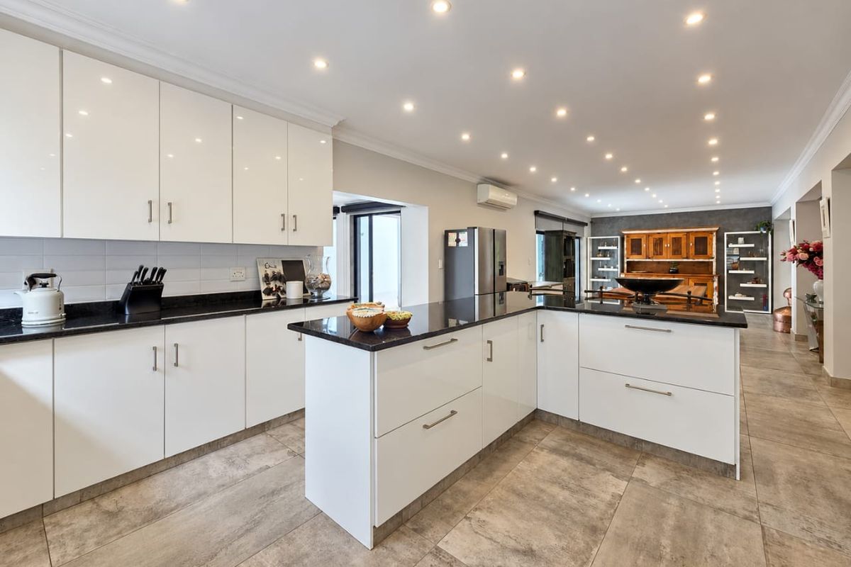 Modern kitchen featuring glossy white cabinetry, black granite countertops, a central island, and tiled flooring, illuminated by recessed downlights.